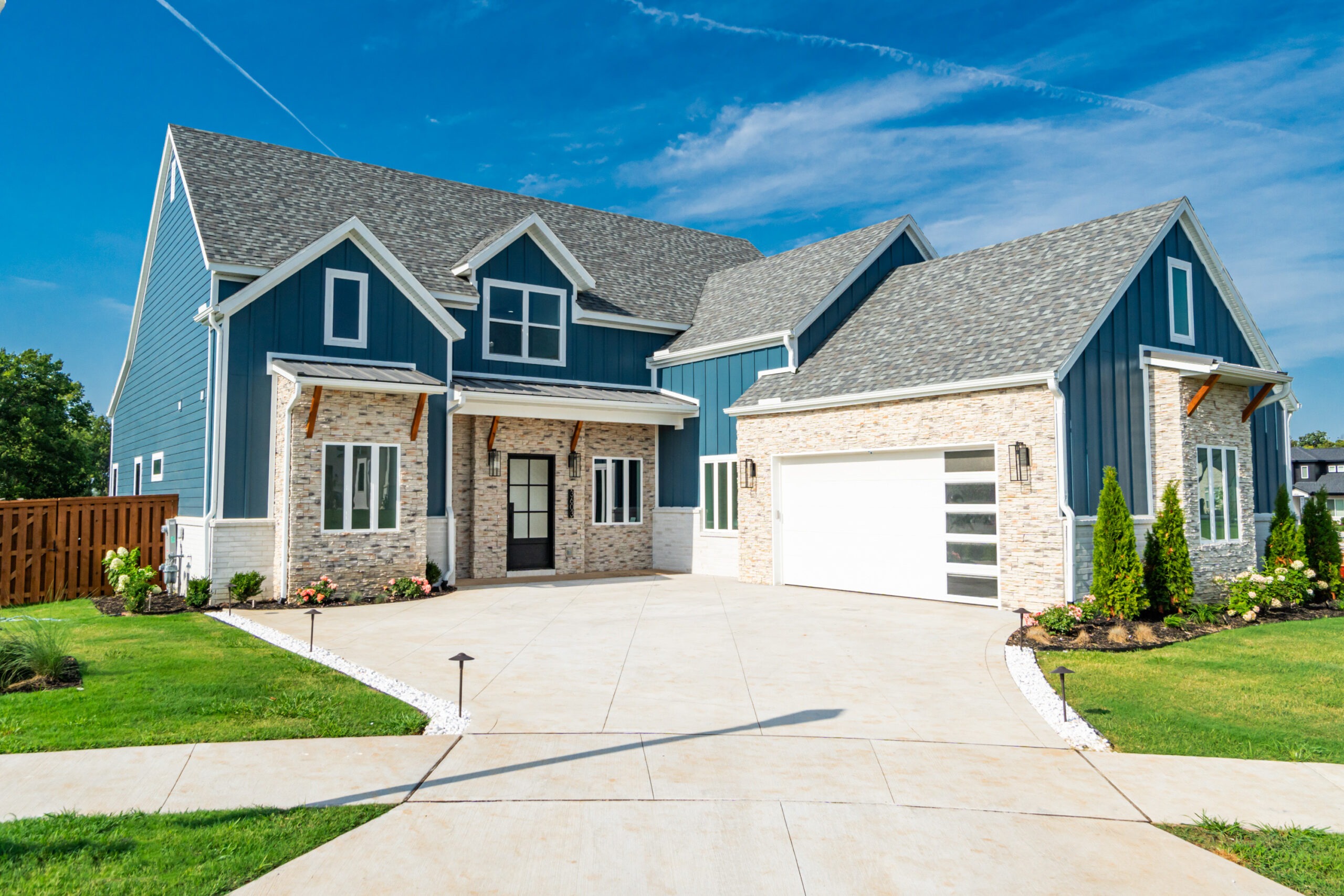 Modern residential home with blue siding and stone accents, featuring a spacious driveway and landscaped garden, representing Leadership Properties' commitment to quality community living in Northwest Arkansas.