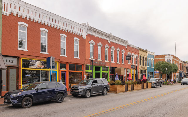 Historic downtown Bentonville street featuring vibrant storefronts, parked vehicles, and outdoor dining, highlighting the community's blend of urban convenience and local charm near Echelon residences.